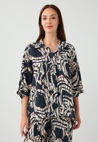 Camicia a manica lunga, modello oversize, in blu navy e crema con motivi astratti. Realizzata in tessuto leggero con una consistenza morbida e maniche a tre quarti.