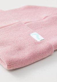 Bonnet en tricot rose fait de tissu doux et texturé, présentant un ourlet replié et une petite étiquette blanche avec des détails turquoise.