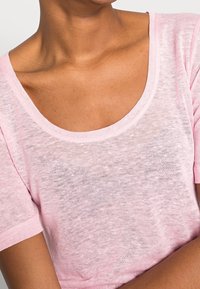 Light pink, short-sleeve t-shirt with a wide scoop neckline; made of a sheer, soft fabric with a slightly textured finish.