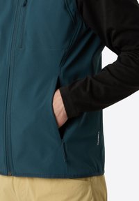 Teal stofjakke med en sort langærmet inderside, der har sidelommer, lynlås lukning og et 'WINDWALL'-mærke på den nederste side.