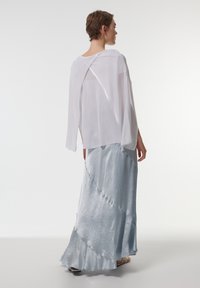 Luchtige witte doorzichtige top met een split aan de achterkant, gecombineerd met een lichtblauwe satijnen maxi rok met een gestructureerd, gelaagd ontwerp en een gekartelde zoom.