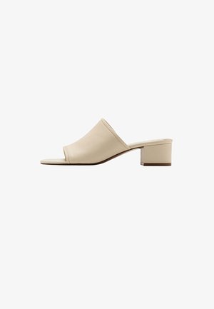 Sandalia mule beige con punta abierta, tacón bajo de bloque y parte superior de cuero suave, mostrada de perfil sobre fondo blanco.
