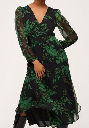 Robe noire à motifs floraux avec des manches longues transparentes, un décolleté en V et une taille cintrée. Motifs botaniques verts dominants sur l'ensemble.