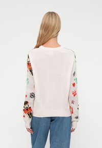 Helles rosa Sweatshirt mit bunten, urlaubsinspirierten Mustern an den Ärmeln, die Schneeflocken, Geschenke und Nussknackerdesigns zeigen. Weicher Stoff.