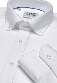 Chemise blanche ajustée en tissu texturé, avec un col à boutonnière et des accents bleus contrastants à l'intérieur du col. Équipée de boutons blancs.