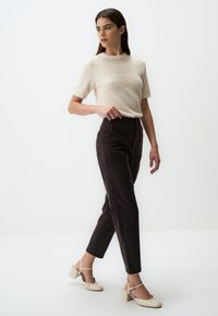 Lichtbeige trui met korte mouwen en een gestructureerde bovenkant en decoratieve stiksels, gecombineerd met hoog-geplaatste donkerbruine broek en neutrale blokkant schoenen.