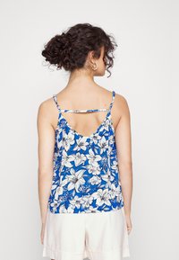 Top de tanque azul floral com alças finas, apresentando um design de costas baixas e um corte solto. O material tem uma textura suave com padrões de flores brancas.