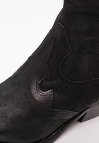 Zbliżenie czarnego skórzanego buta kowbojskiego z ozdobnymi haftowanymi wzorami i niskim obcasem na białym tle.