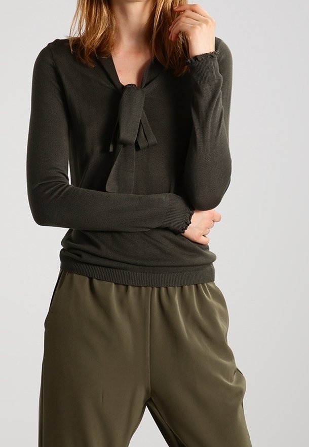 Mörkgrön tröja med knytdetalj vid halsringningen, ribbade ärmslut och en figursydd design, kombinerad med lösa olivgröna byxor.