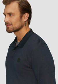Marinepolo met een gestructureerde stof, voorzien van een kraag en een klein zwart merkembleem op de borst. Glad, aansluitend ontwerp.