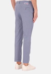 Lichtblauwe, slim-fit broeken gemaakt van een rekbaar materiaal. Heeft een achterzak, minimale stiksels en wordt gedragen met witte sneakers.