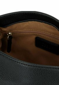 Interno della borsa a tracolla in pelle nera con rivestimento in tessuto beige. Presenta una tasca con cerniera e un'etichetta nera.