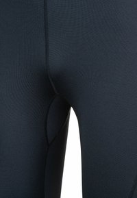 Mustat legginsit, joissa on sileä ja joustava pinta, fyysinen muotoilu ja litteät saumat, näkyvät reidestä vyötäröön.