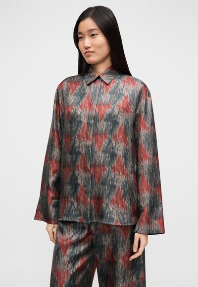 Langærmet skjorte i et silkelignende stof med et flerfarvet geometrisk mønster i rød, grå og sort. Klassisk krave og afslappet pasform.