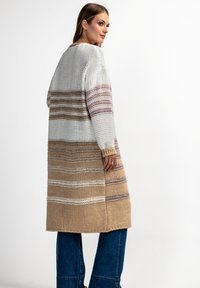 Sweter o swobodnym kroju, w białe, beżowe i mauve prążki. Posiada długie rękawy oraz teksturowany materiał z różnymi wzorami ściegów.