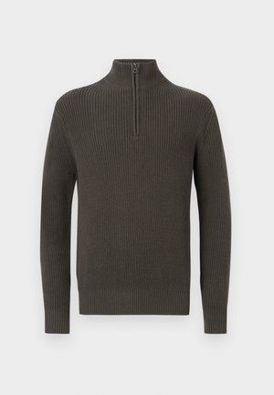 Tamsiai žalia raukšlėta megztinis su aukštu apykakle ir pusės užtrauktuku. Yra ilgos rankovės ir tekstūruota megztinė struktūra.