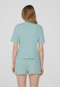 Conjunto de top y pantalones cortos de punto azul claro con bordes volados, mangas cortas y un ajuste relajado. La tela tiene un aspecto texturizado.
