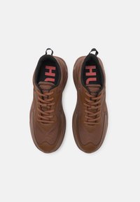 Ruske tennarit z mrežastim in sintetičnim zgornjim delom, okroglo konico, vezalno zasnovo, črno notranjost ter izrazitim rdečim logotipom "HUGO" na jeziku.