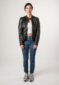 Zwarte leren motorjack met een hoge kraag, een ritssluiting aan de voorkant en geribde schouderaccenten, gecombineerd met blauwe jeans en sneakers.