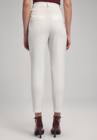 White tailored trousers with a slim fit, featuring two back pockets and a smooth texture. Paired with burgundy high-heeled shoes.