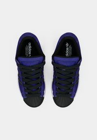 Μωβ και μαύρα αθλητικά παπούτσια με καουτσούκ προστατευτικό στη μύτη, με μαύρα κορδόνια και σήμανση Adidas στη γλώσσα και την εσωτερική σόλα.