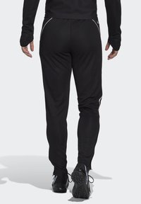 Zwarte sportbroek met een taperende pasvorm, voorzien van witte accentstrepen langs de zijkanten, gemaakt van soepel, lichtgewicht materiaal.