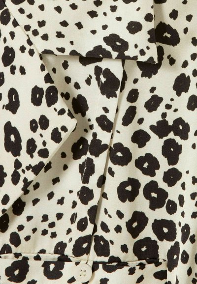 Estampado de leopardo negro sobre tela beige claro, con un cuello y un detalle de botón en la parte inferior, que muestra una textura suave y un diseño en capas.
