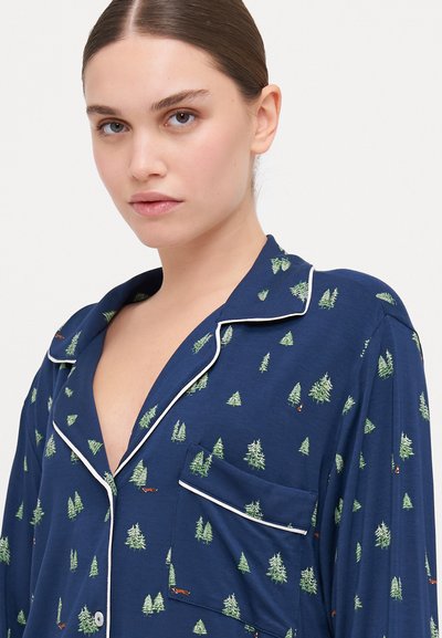 Navy blue pajama top with a green tree pattern, white accents along the collar and pocket, and a soft fabric texture.