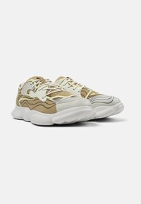 Beige sneakers with textured panels, white accents, and thick, cushioned soles. Features contrasting wave patterns and lace-up design.