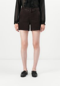 Shorts en velours côtelé marron avec une taille haute ceinturée, deux poches latérales et une coupe droite, associés à des chaussures noires à lacets.