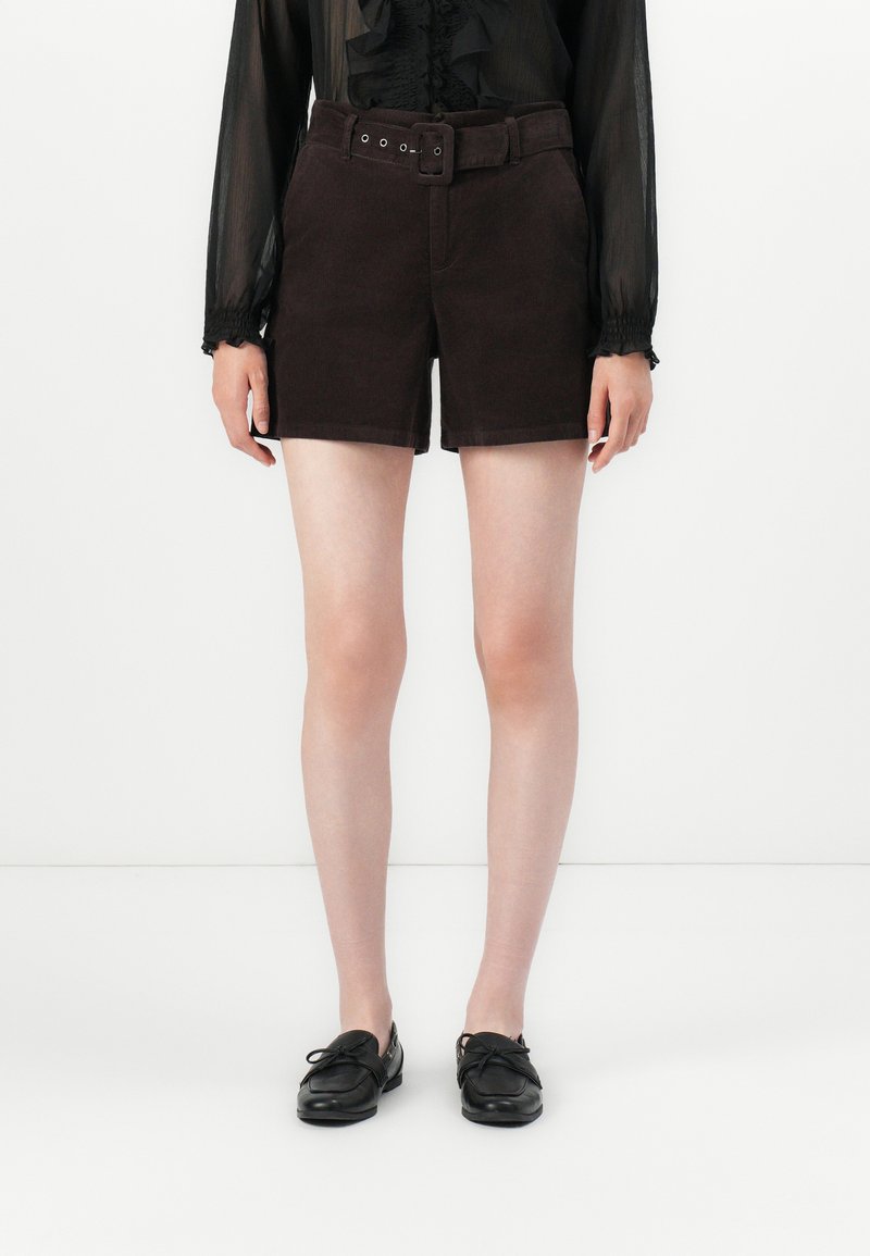 Shorts en velours côtelé marron avec une taille haute ceinturée, deux poches latérales et une coupe droite, associés à des chaussures noires à lacets.