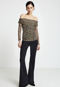 Leopardenmuster-Off-Shoulder-Oberteil mit langen, transparenten Ärmeln; kombiniert mit schwarzen ausgestellten Hosen; schlanke Silhouette und glatte Stoffstruktur.