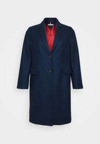 Cappotto lungo blu navy con chiusura a un bottone e due tasche frontali, con fodera rossa visibile al colletto e all'apertura.