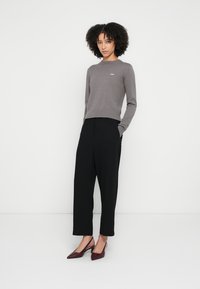 Grå genser med lange ermer og ribbekanter, kombinert med svarte vidbukser og burgunder pumps med spiss tå. Enkel logodetalj på genseren.