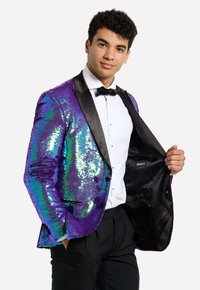 Blazer viola con paillettes iridescenti, revers in satin nero e bottoni. Indossato sopra una camicia bianca e un papillon nero.