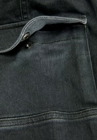 Bolsa de mezclilla negra con solapa y cierre de botón. La tela presenta una textura suave con sutiles detalles de costura.