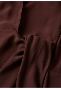 Ruskea, kevyt kangas, jolla on sileä texture, pehmeillä laskoksilla ja roikkumisella. Ei näkyviä kuvioita tai kiinnikkeitä.