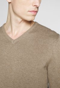 Suéter marrón de cuello en V con una textura acanalada y diseño ajustado. La tela suave presenta costuras lisas y un escote limpio.