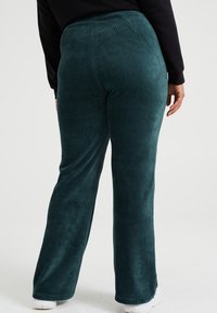 Spodnie sztruksowe w ciemnym teal, z szerokimi nogawkami i pionowym teksturem prążkowanym. Elastyczny pas dla wygody.