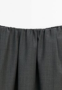 Tissu gris foncé avec une ceinture élastique et des plis froncés, montrant la zone de la taille d'un vêtement sur un fond blanc.