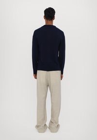 Námořnický pletený svetr s uvolněným střihem, doplněný světlobéžovými volnými kalhotami. Měkká textura a jemné designové detaily jsou viditelné.