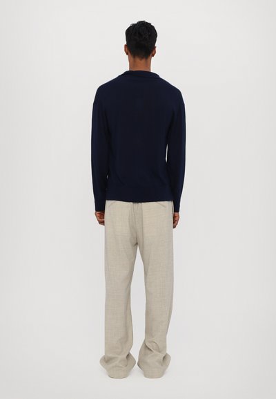 Maglione a maglia navy con vestibilità rilassata, abbinato a pantaloni beige chiaro e larghi. Texture morbida e dettagli di design sottili visibili.