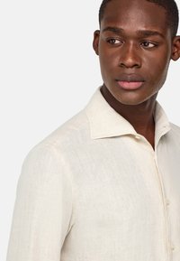 Camicia di lino beige chiaro con colletto button-down, caratterizzata da un tessuto testurizzato e sottili variazioni di colore per un maggiore profondità.