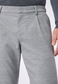 Pantaloni a scacchi grigi con una texture liscia, caratterizzati da una parte anteriore piatta e passanti per la cintura. Il motivo è composto da linee alternate chiare e scure.