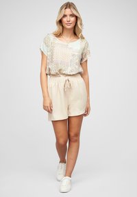 Haut léger et à motifs avec des manches courtes, associé à un short beige à cordon de serrage. Des baskets blanches complètent la tenue.