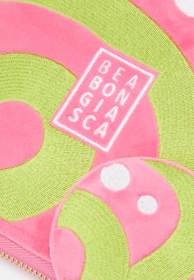 Pink and green plush pouch featuring circular patterns and a textured surface, with a branded label in white, surrounded by contrasting colors.