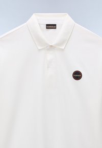 Valkoinen polo-paita, joka on valmistettu puuvillasta. Paita sisältää klassisen kauluksen, kahden napin nappilistan ja pyöreän logo-patchin vasemmassa rinnassa.
