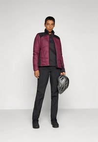 Kurtka bordowa z ociepleniem i czarnymi detalami, w zestawie z czarną, długorękawową bluzką i czarnymi spodniami. Na głowie szary kask rowerowy.