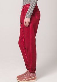 Sarkans kokvilnas sporta bikses ar auklu viduklī, elastīgiem piedurknēm un sānu kabatām. Saskaņotas ar gaiši rozā sporta apaviem.