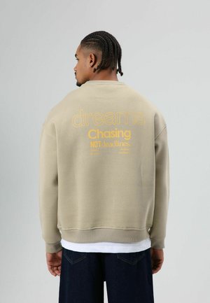 Beige katoenen sweatshirt met op de rug de gele opdruk "dreams Chasing NOT deadlines". Geribbelde boorden en zoom. Casual pasvorm.